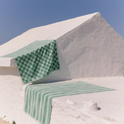Green checkered beach towel on a white stone surface with a clear blue sky.