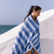 Woman wrapped in a blue striped beach towel against a white wall with ocean view