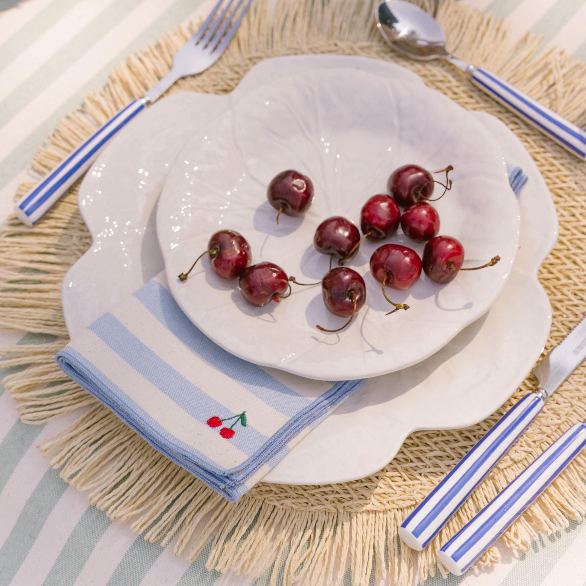 White plate with cherries on a woven placemat with striped napkin, with a cherry design.