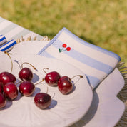 Cherries on a plate with a striped napkin featuring red cherry embroidery, outdoors.