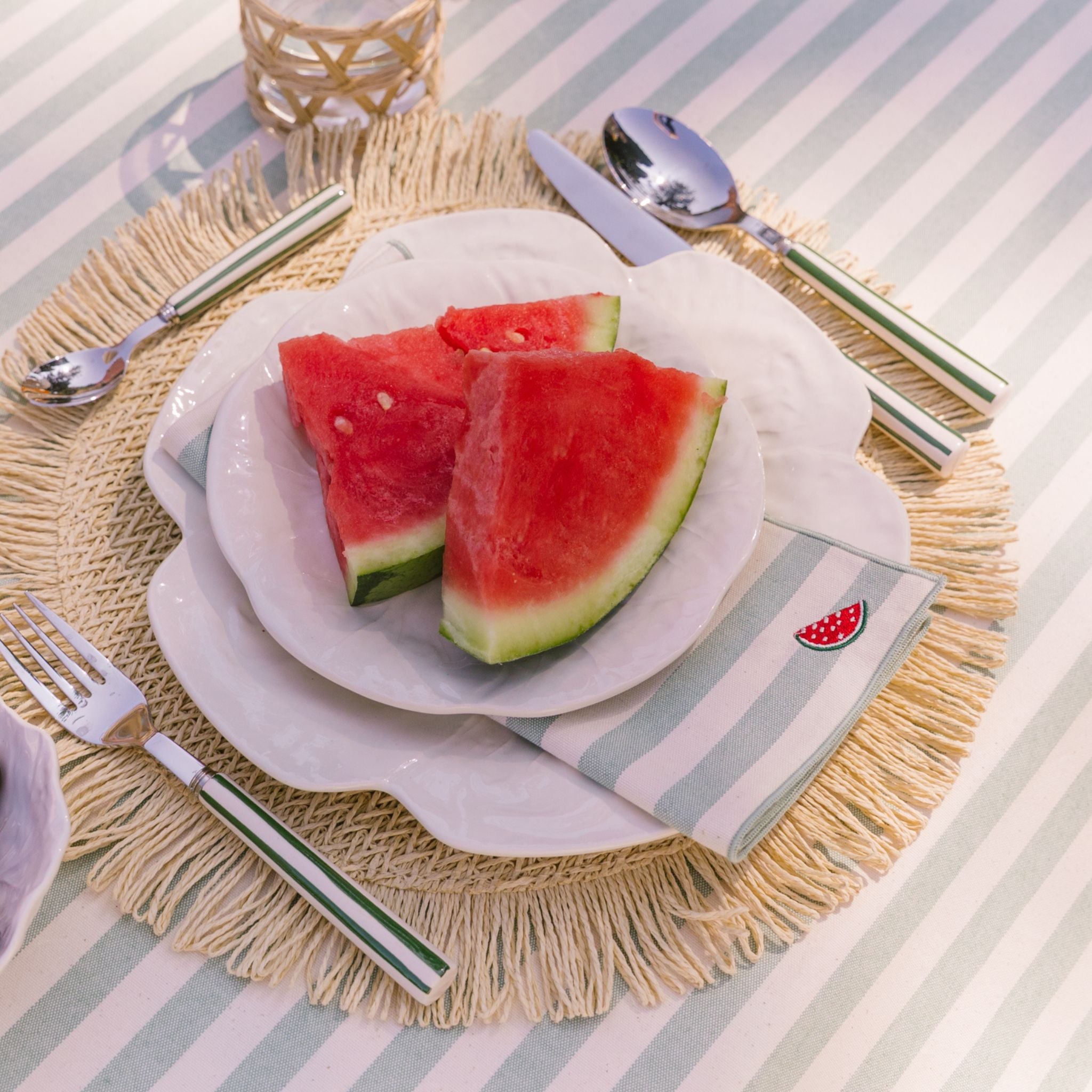 Slices of watermelon on a plate with a striped tablecloth and napkin.