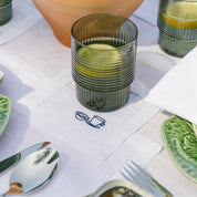Green glass with a textured design on a white tablecloth with cutlery and plates.