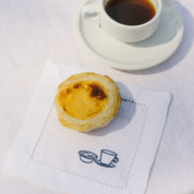 Pastel de nata (Portuguese egg tart) on a white napkin with a cup of coffee in the background.