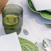 Green glass with lemon slices on a table setting with plates and cutlery.