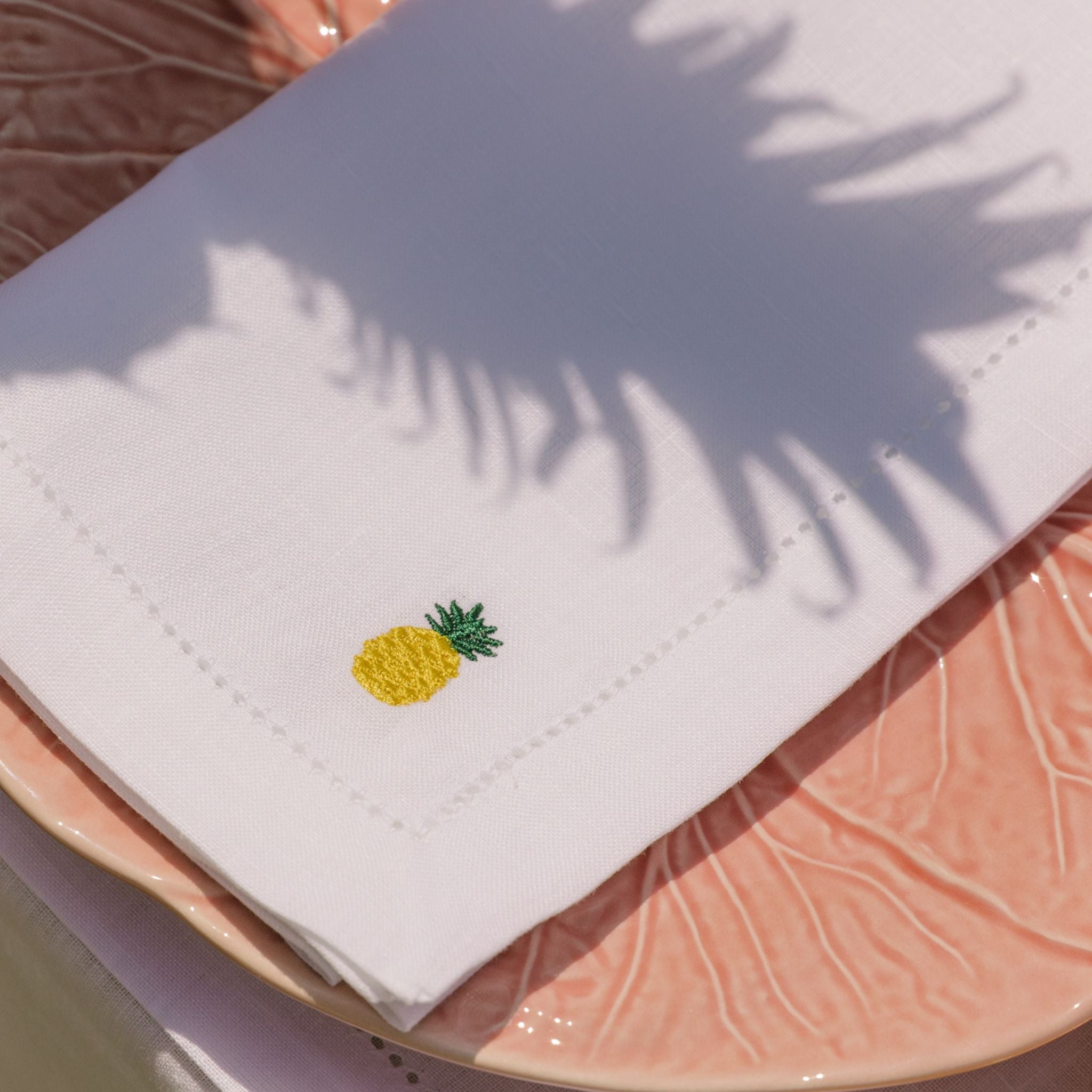 White napkin with a pineapple embroidery on a pink plate