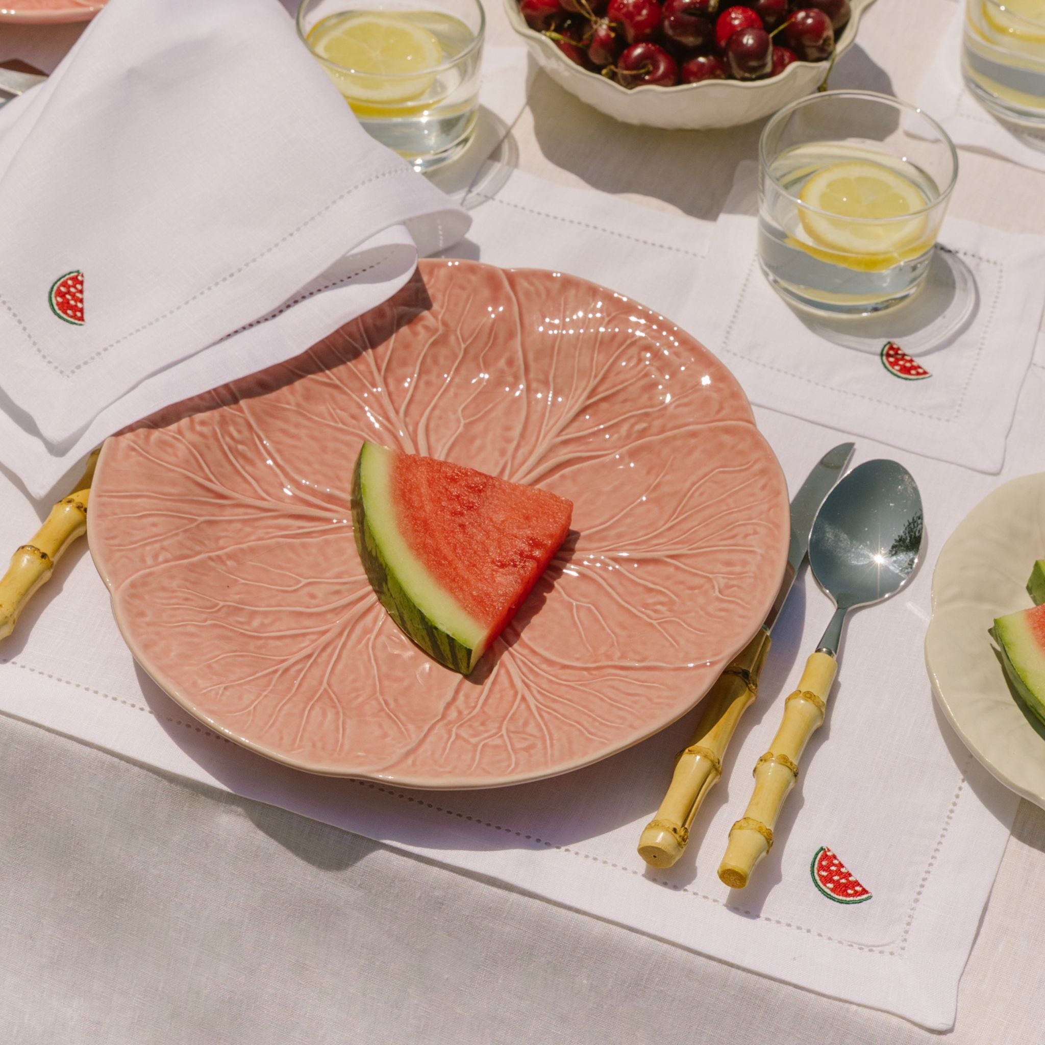 Pink decorative plate with watermelon slice on a table setting with glasses and cutlery.
