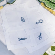 White cocktail napkins with blue embroidered designs on a white surface