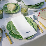 Table setting with green ceramic plates, white napkin, and bamboo cutlery on a white tablecloth.