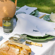 Outdoor dining setup with bread, olive oil, and green plates on a white tablecloth.