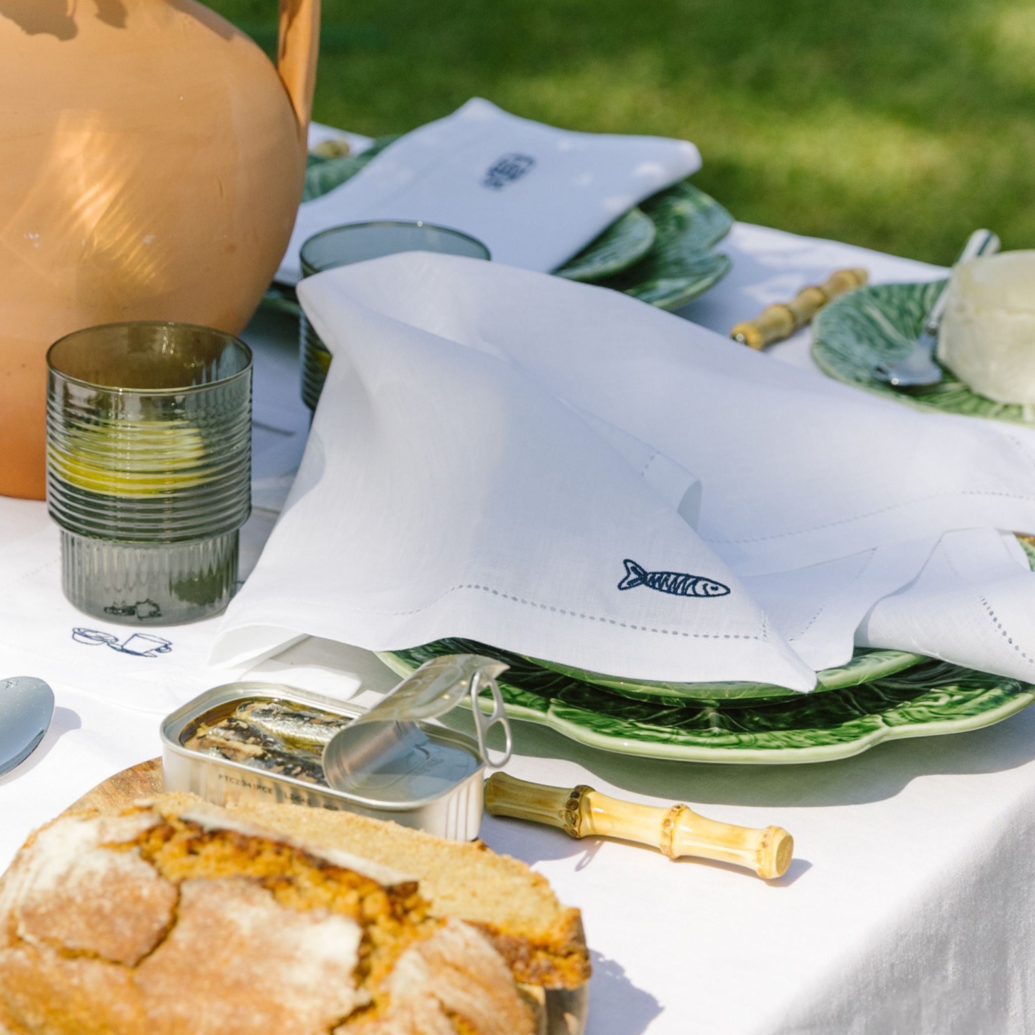 Outdoor dining setup with bread, olive oil, and green plates on a white tablecloth.