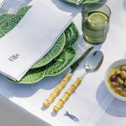 Table setting with green plates, bamboo cutlery, and a glass of water with lemon.