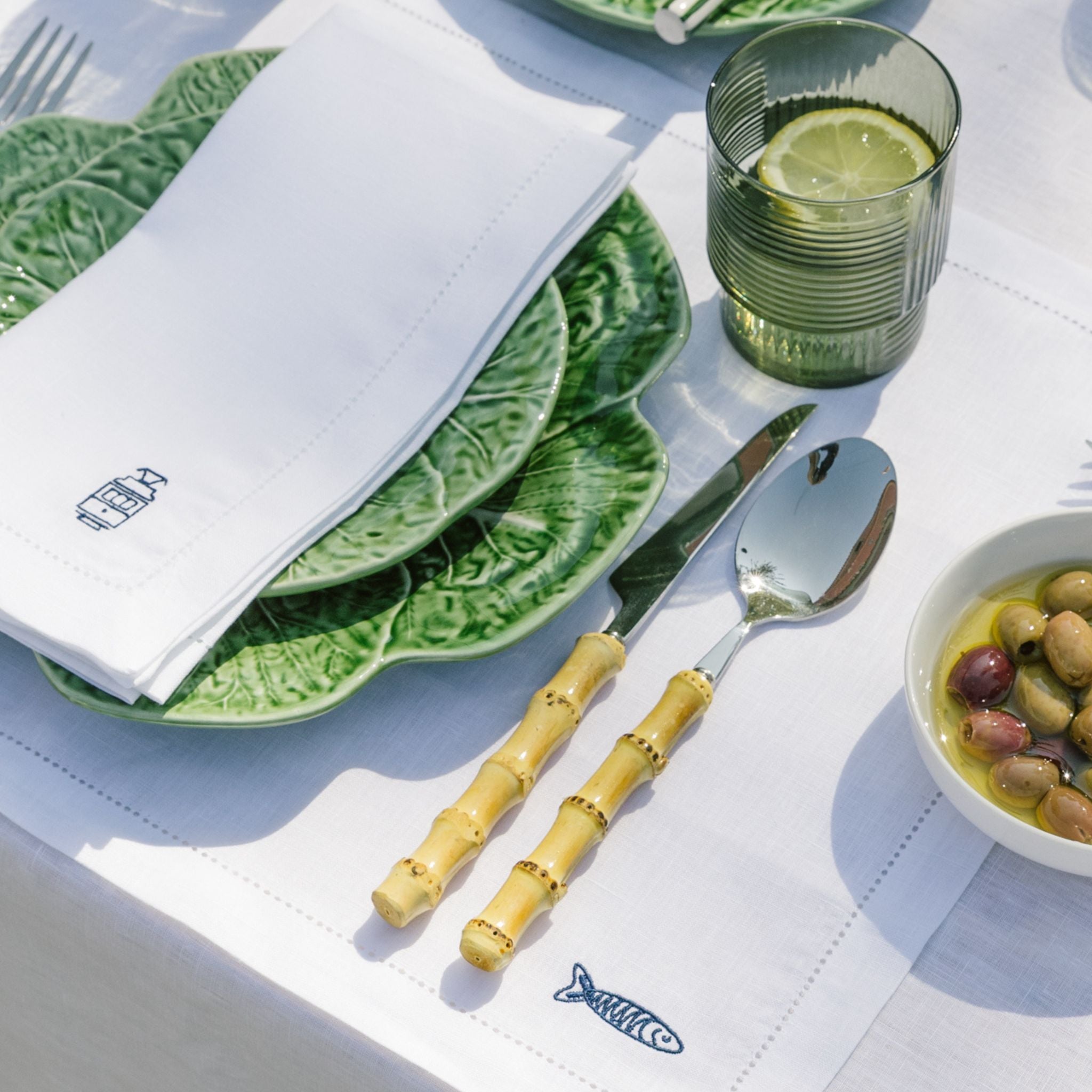 Table setting with green plates, bamboo cutlery, and a glass of water with lemon.