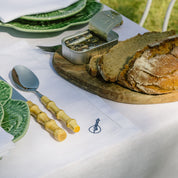 Table setting with bread, butter, and cutlery on a white tablecloth with green leaf plates.